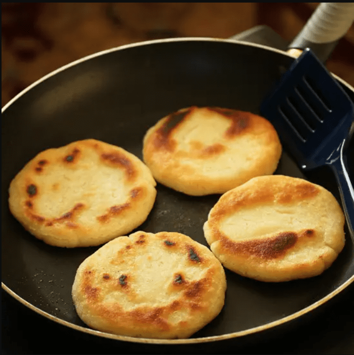 Four small pancakes are in a pan with a spatula.