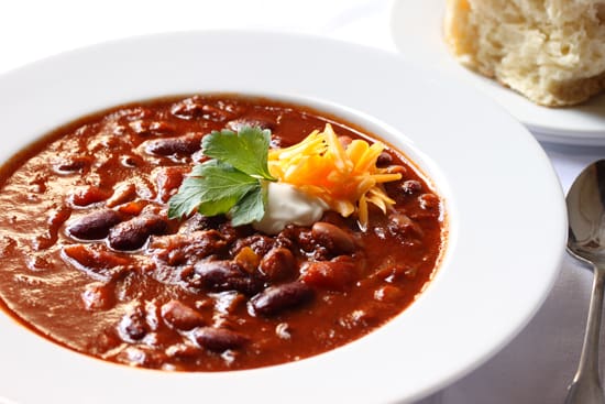 A bowl of chili with cheese and cilantro.