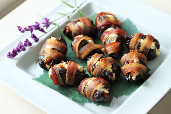 A plate of bacon wrapped dates on top of a green leaf.