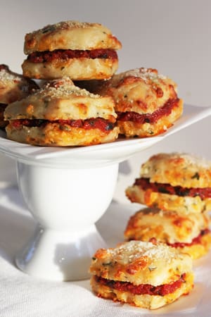 A white plate topped with several sandwiches covered in cheese.