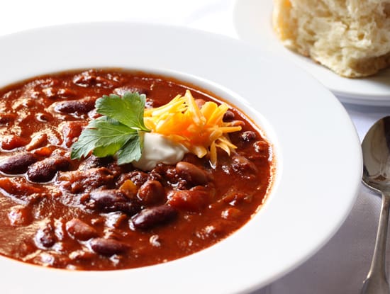 A bowl of chili with cheese and cilantro.