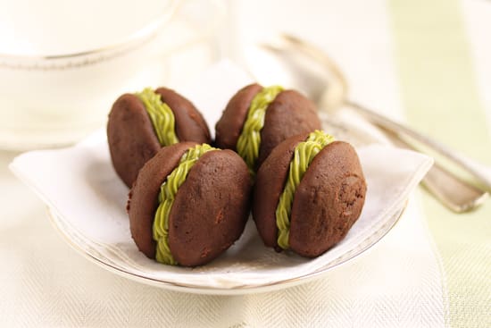 Four chocolate cookies with green frosting on a plate.