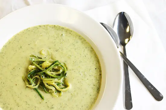 A bowl of soup with zucchini noodles on top.