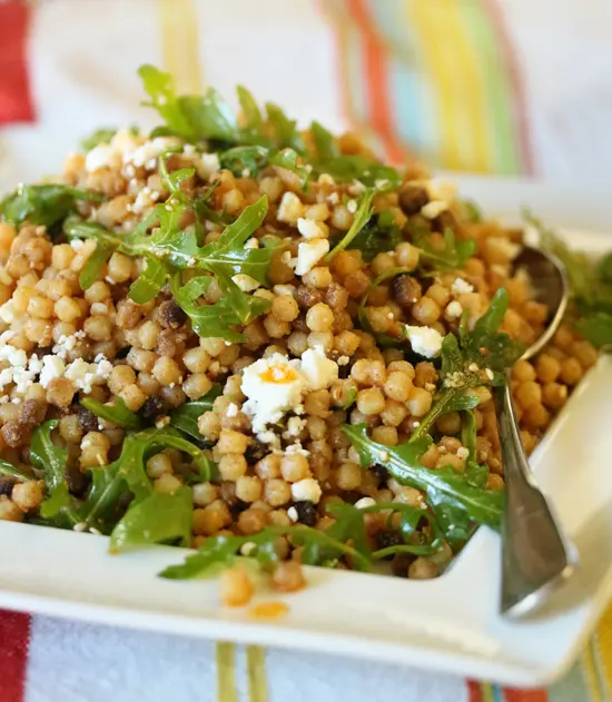 A white plate topped with couscous and greens.