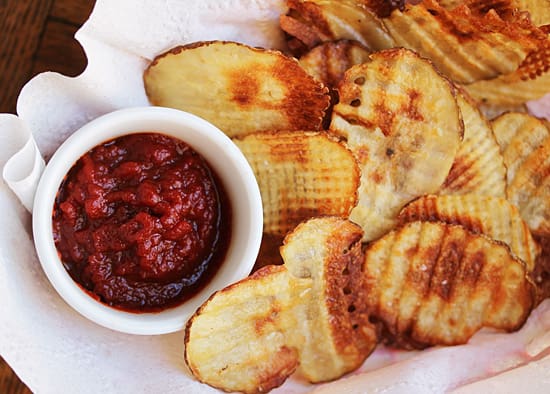 A bowl of salsa next to some grilled potatoes.