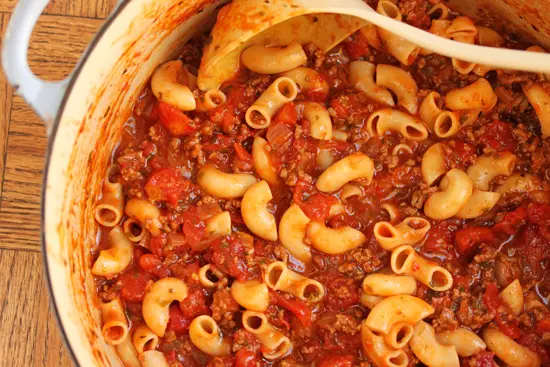A bowl of macaroni and chili with a spoon.