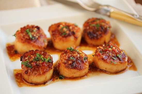 A plate of scallops with sauce and parsley.
