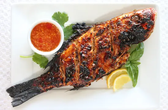 A plate of fish with sauce and lemon.