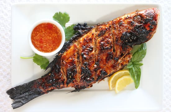 A plate of fish with sauce and lemon.