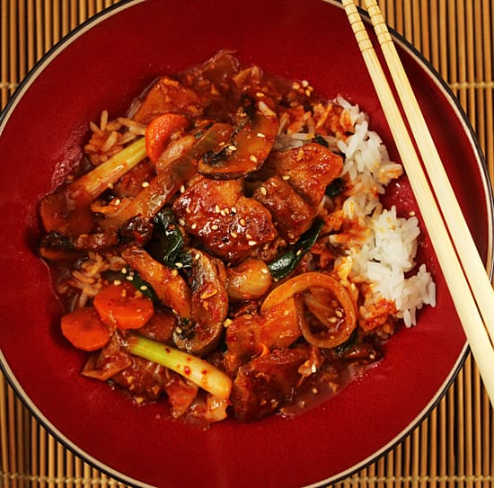 A red bowl of food with chopsticks on the side.