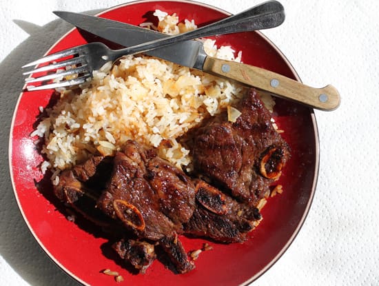 A red bowl of rice and meat with a fork, knife and spoon.