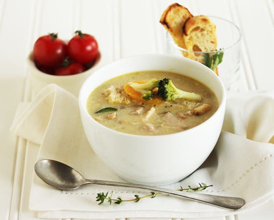 A bowl of soup with spoon and tomatoes on the side.