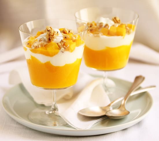 Two glasses of dessert on a plate with spoons.