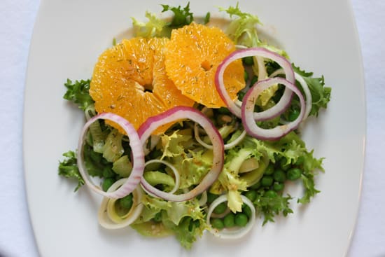 A salad with orange slices and onions on top.