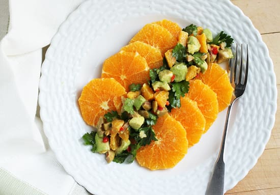 A white plate topped with sliced oranges and salad.