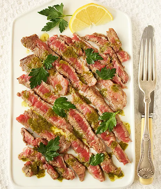 A white plate topped with steak covered in sauce.