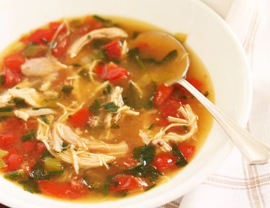 A bowl of soup with chicken and tomatoes.