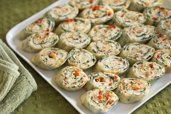 A tray of rolled up cheese and vegetable sandwiches.