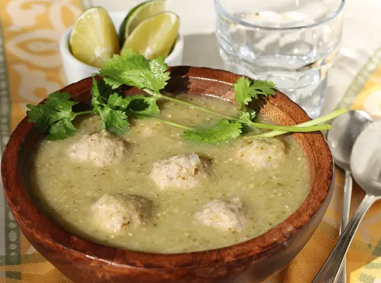 A bowl of soup with meatballs and cilantro.