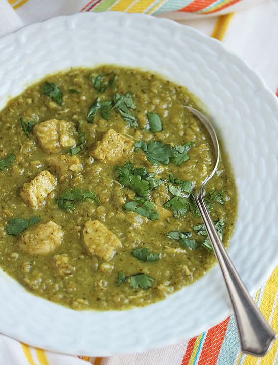 A bowl of green soup with meat and greens.