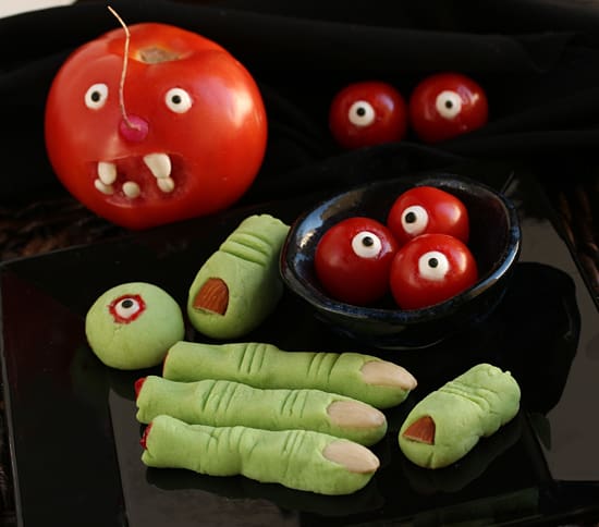 A table topped with green cookies and red tomatoes.