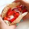 A person holding a tortilla with vegetables in it.