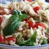 A bowl of pasta salad with tomatoes and basil.