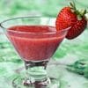 A glass of strawberry juice with a strawberry on the side.