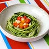 A bowl of green pasta with tomatoes and basil.