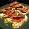 A plate of food with bacon, avocado and tomatoes.